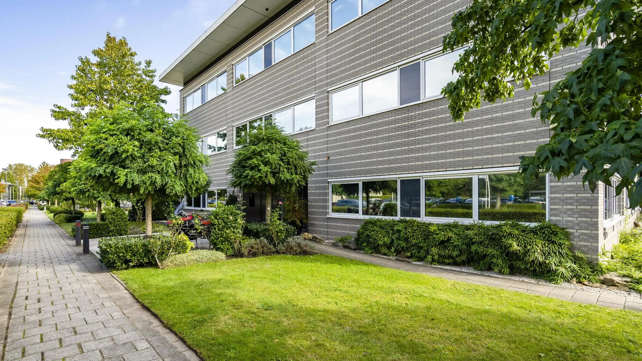 Kantoorpand aan de Jan Leentvaarlaan met moderne gevel, groene voortuin en omliggende bomen.